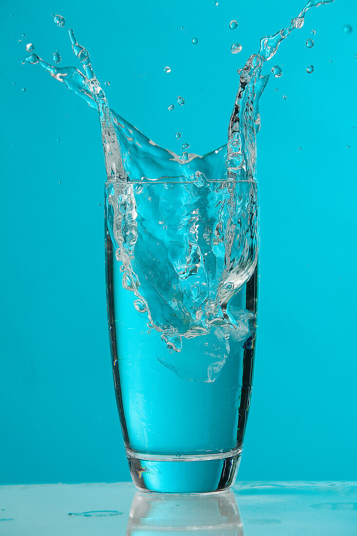 Water Splash As Ice Cube Drops Into Glass Of Water