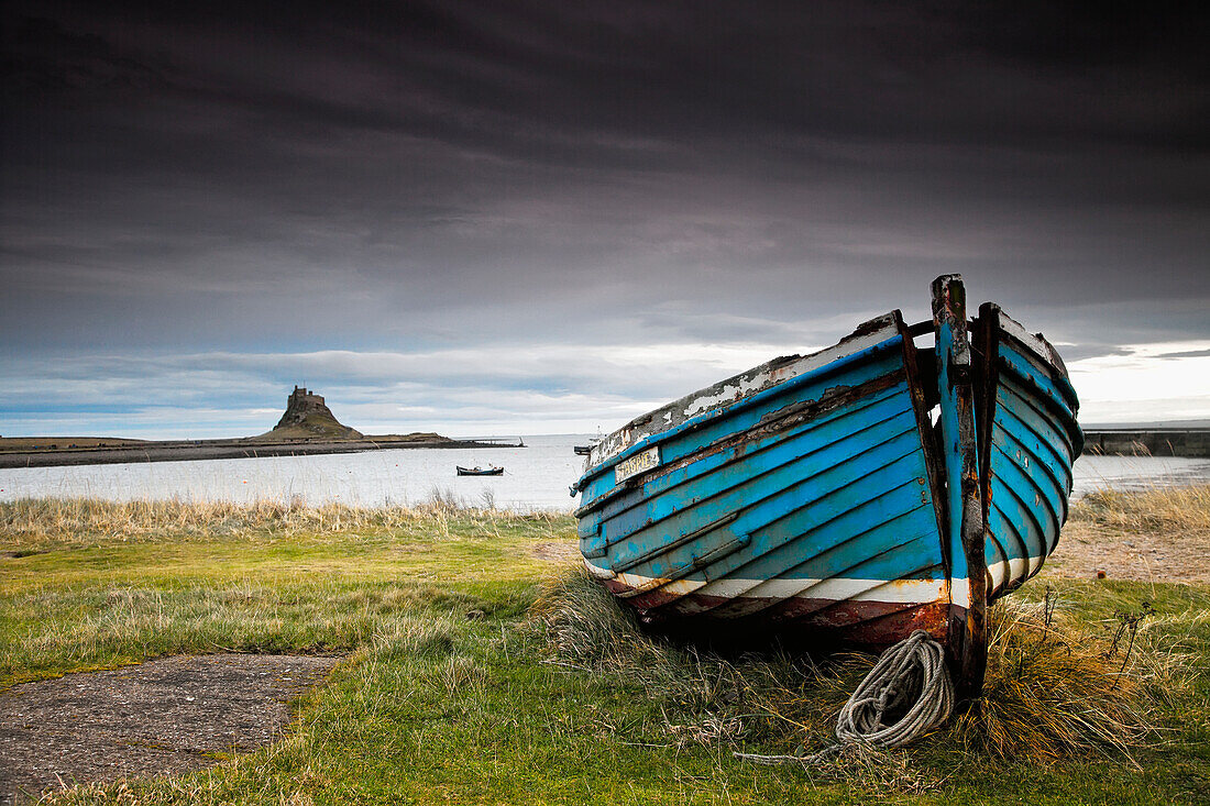 'A Weathered Boat Sitting On The Shore With Lindisfarne Castle In The Distance; Lindisfarne, Northumberland, England'