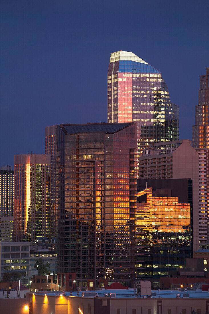 'Calgary Skyline At Dawn With City Lights And Deep Blue Sky With Buildings Reflecting The Orange Glow Of Sunrise; Calgary, Alberta, Canada'