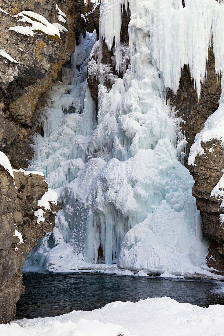 'Frozen Waterfalls With Icicles Snow Covered Cliff And Open Water; Alberta, Canada'