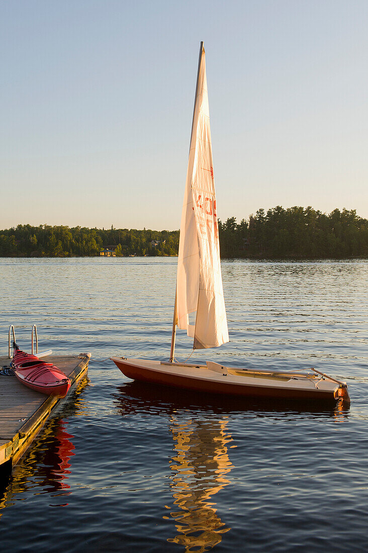 'A Kayak On A Dock And A Sailboat In The Water; Lake Of The Woods, Ontario, Canada'