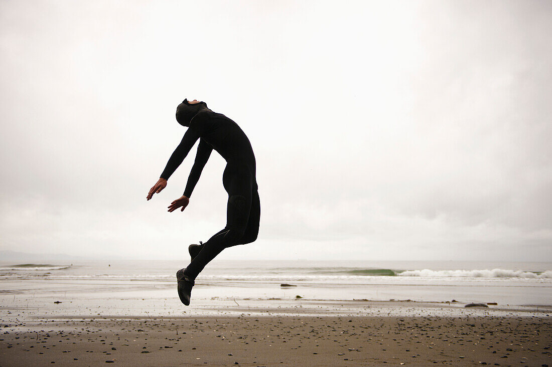 'An Individual Wearing A Wet Suit Jumping In Mid-Air On A Beach; French Beach, British Columbia, Canada'