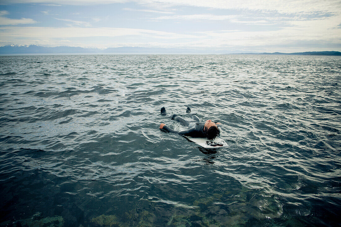 'A Surfer Lays On His Back On His Surfboard In The Water; Victoria, British Columbia, Canada'