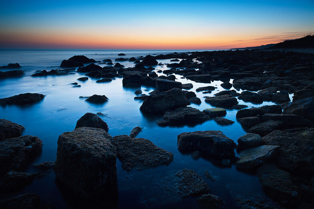 'Rocks In The Tranquil Water Along The Coast At Sunset; Tarifa, Cadiz, Andalusia, Spain'