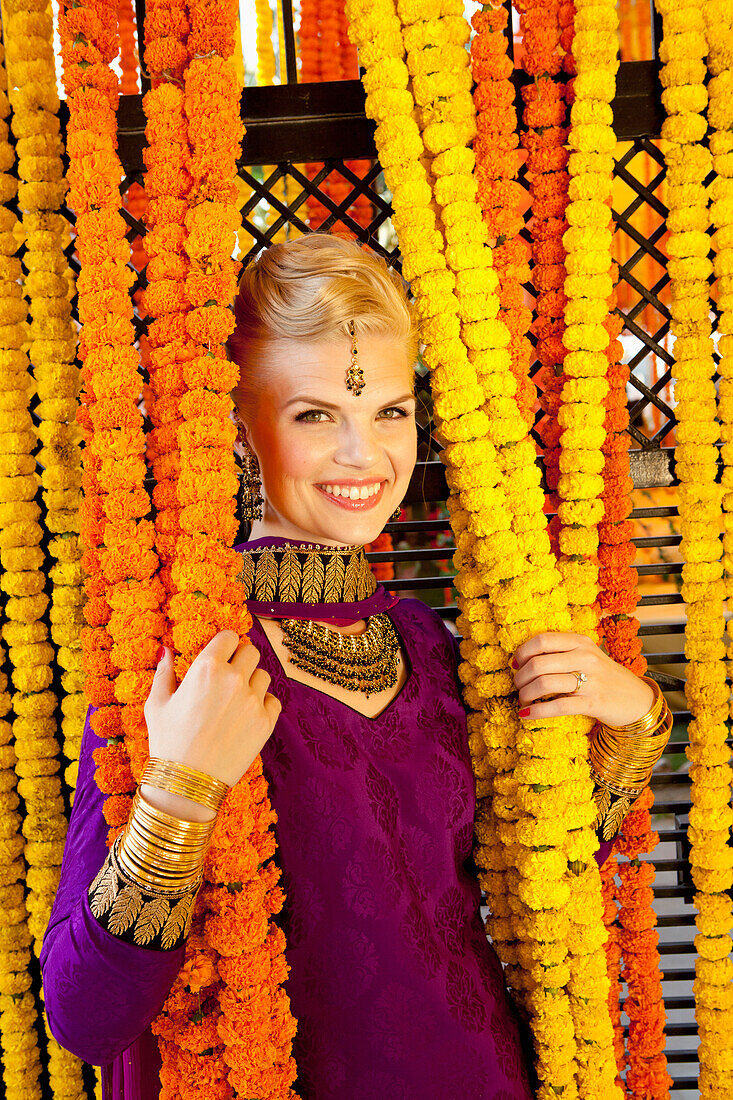 'A Woman Dressed In A Purple Sari Holding Onto The Hanging Strung Flowers; Ludhiana, Punjab, India'