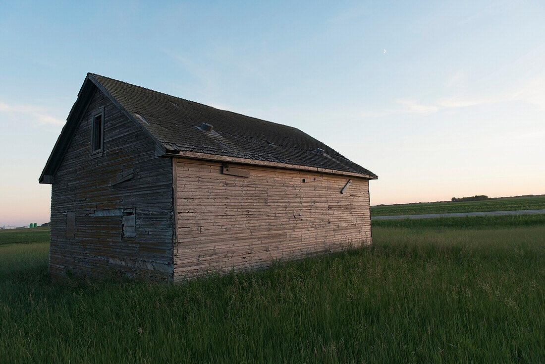 A wooden shed in the middle of a grass field