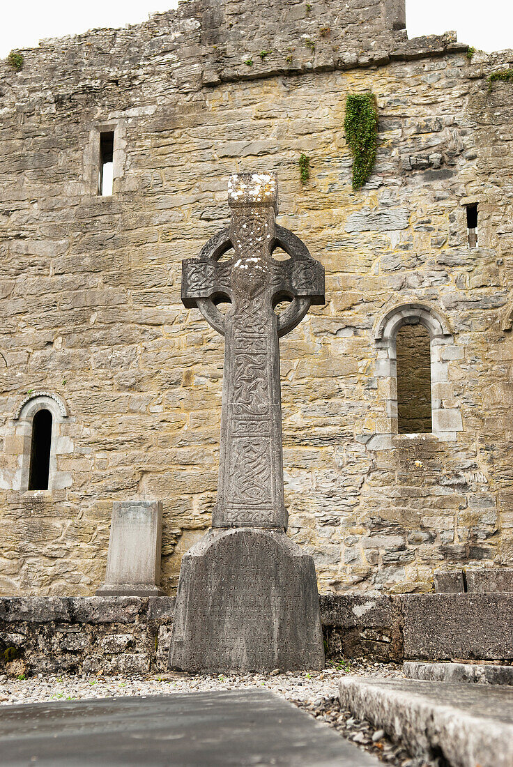 'A large celtic cross monument in front of the ruins of a stone building;Ireland'