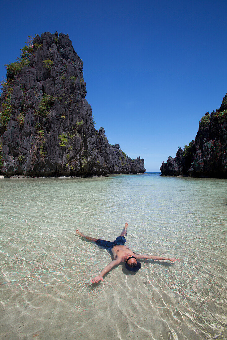 'Man Floating In Clear Water Of Small Lagoon; Miniloc Island, Palawan, Philippines'
