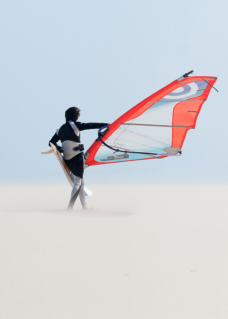 'A Windsurfer Walks On The Sand Of Punta Paloma Beach With His Board; Tarifa, Cadiz, Andalusia, Spain'