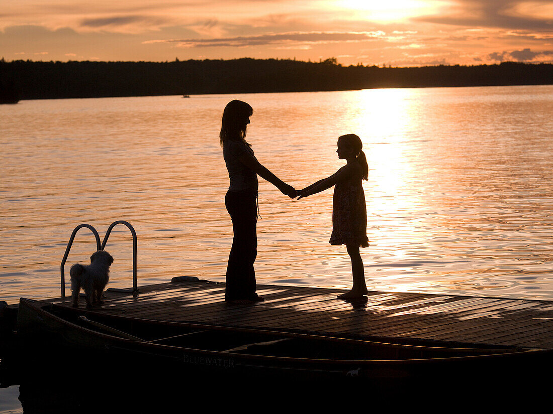 Silhouette Of Mother And Daughter On A Dock, Lake Of The Woods, Ontario, Canada