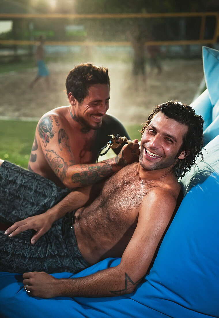 'Two Shirtless Men Laughing With A Beach Volleyball Court In The Background; Tarifa, Cadiz, Andalusia, Spain'