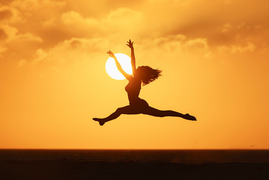 'Silhouette of a woman leaping in the air with the golden sky and sun in the background; Tarifa, Costa de la Luz, Cadiz, Andalusia, Spain'