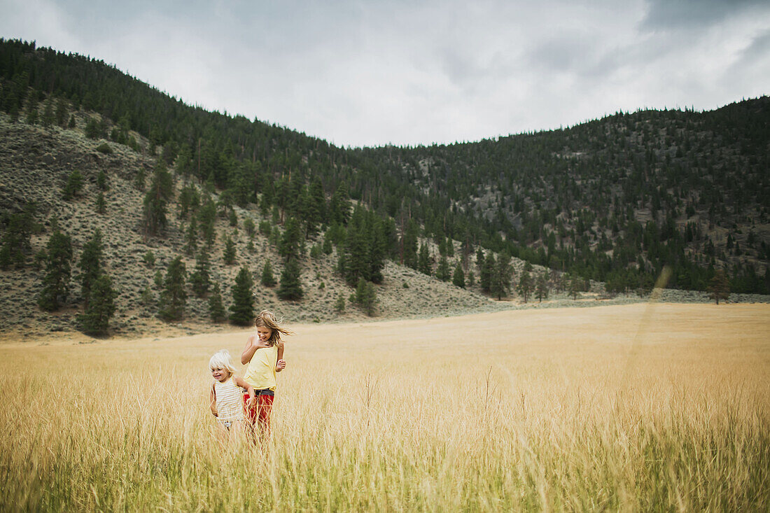 'Two young girls walking in the tall grass of a field; Peachland, British Columbia, Canada'