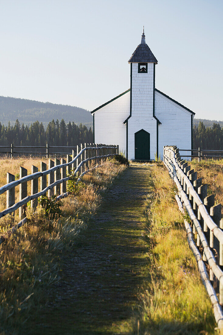 'Old wooden church in foothills with wooden fence and blue sky; Cochrane, Alberta, Canada'