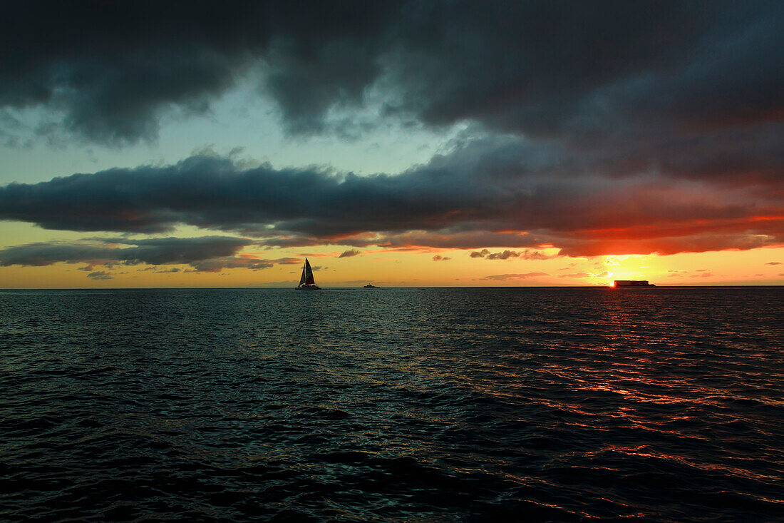 'A sailboat on the ocean water off the coast of Waikiki at sunset; Waikiki, Oahu, Hawaii, United States of America'