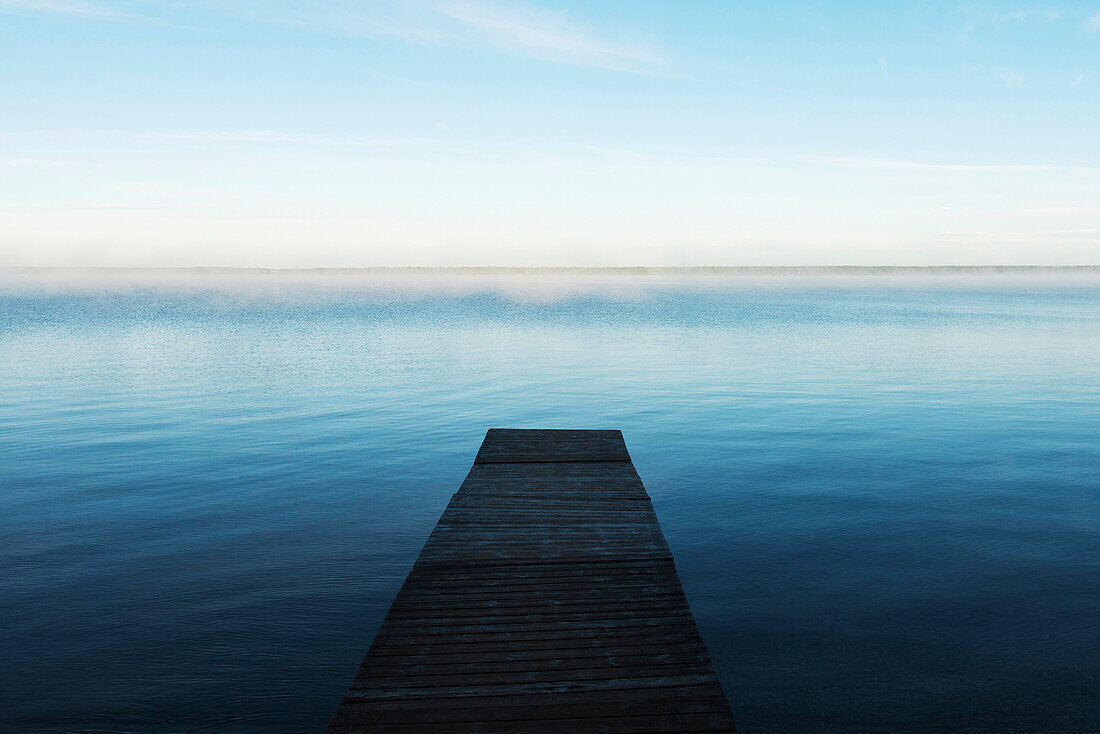 'A wooden dock leading out to a misty tranquil lake in Riding Mountain National Park; Wasagaming, Manitoba, Canada'