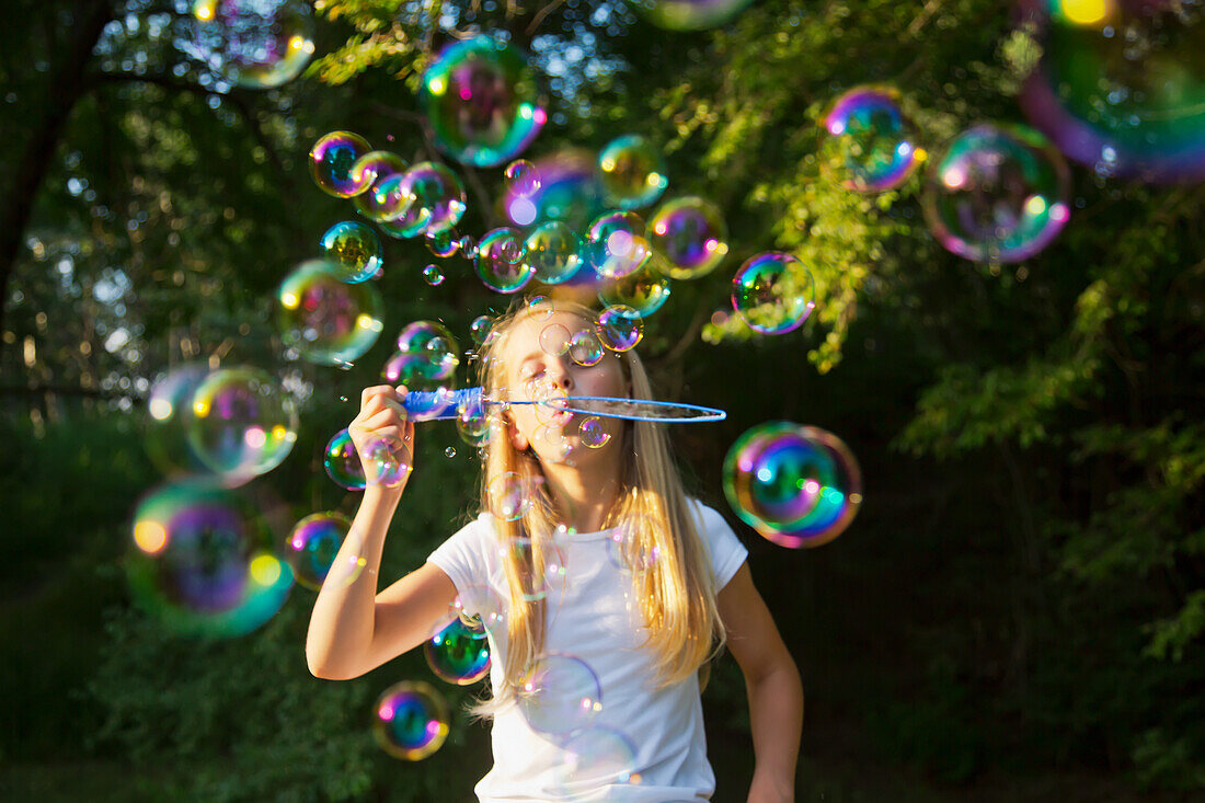 'Young girl blowing bubbles in a park; St. Albert, Alberta, Canada'