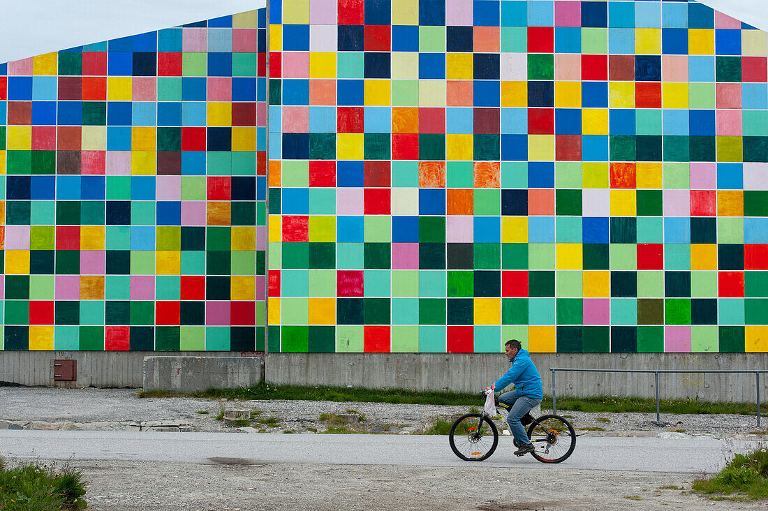 Cyclist passing a building with colorful squares, Nuuk, Greenland