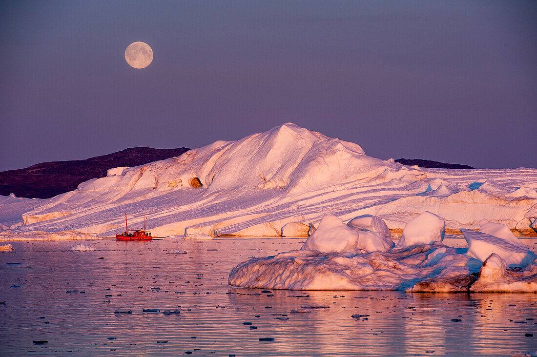 Full moon above fishing boat in front of icebergs in twilight, Ilulissat Icefjord, Ilulissat, Qaasuitsup, Greenland