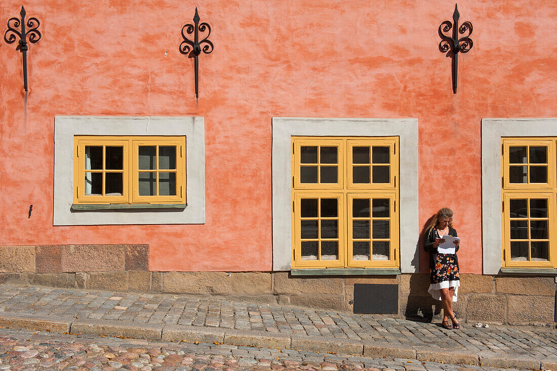 Frau lehnt an einer Hauswand und liest, Gamla Stan, Stockholm, Schweden
