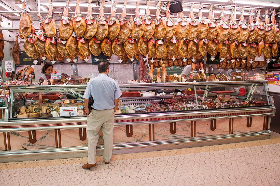 Schinken hängen in einem Metzgerstand in einer Markthalle, Valencia, Valencia, Spanien