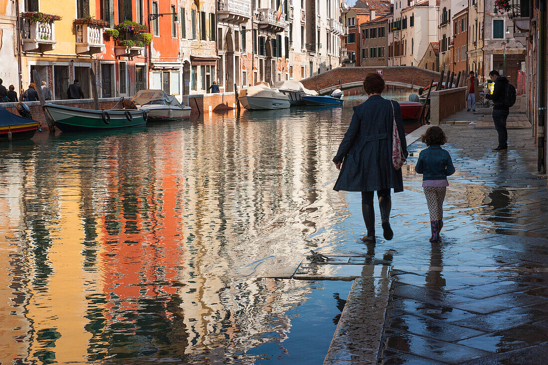 Mutter und Tochter laufen über einen Bürgersteig bei Acqua alta, Venedig, Venetien, Italien