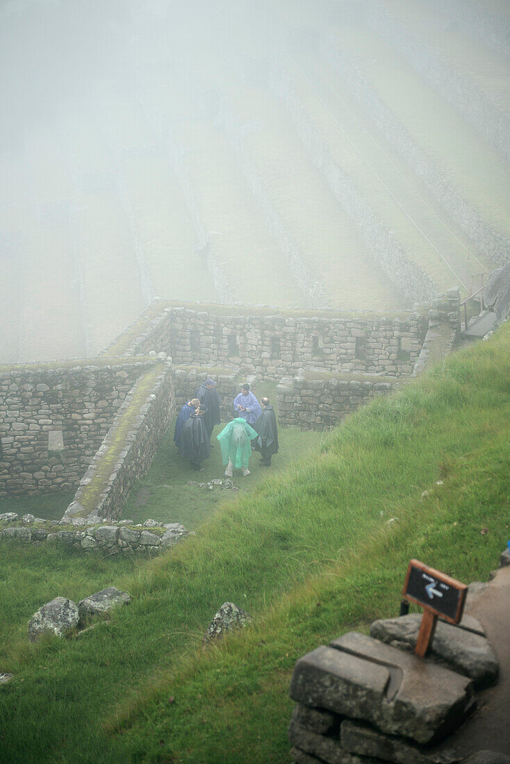 eine Gruppe von Touristen steht zwischen den Ruinen von Machu Picchu eingehüllt in Nebel und Regenkleidung, Aguas Calientes, Peru, Süd Amerika, 7 Neue Weltwunder