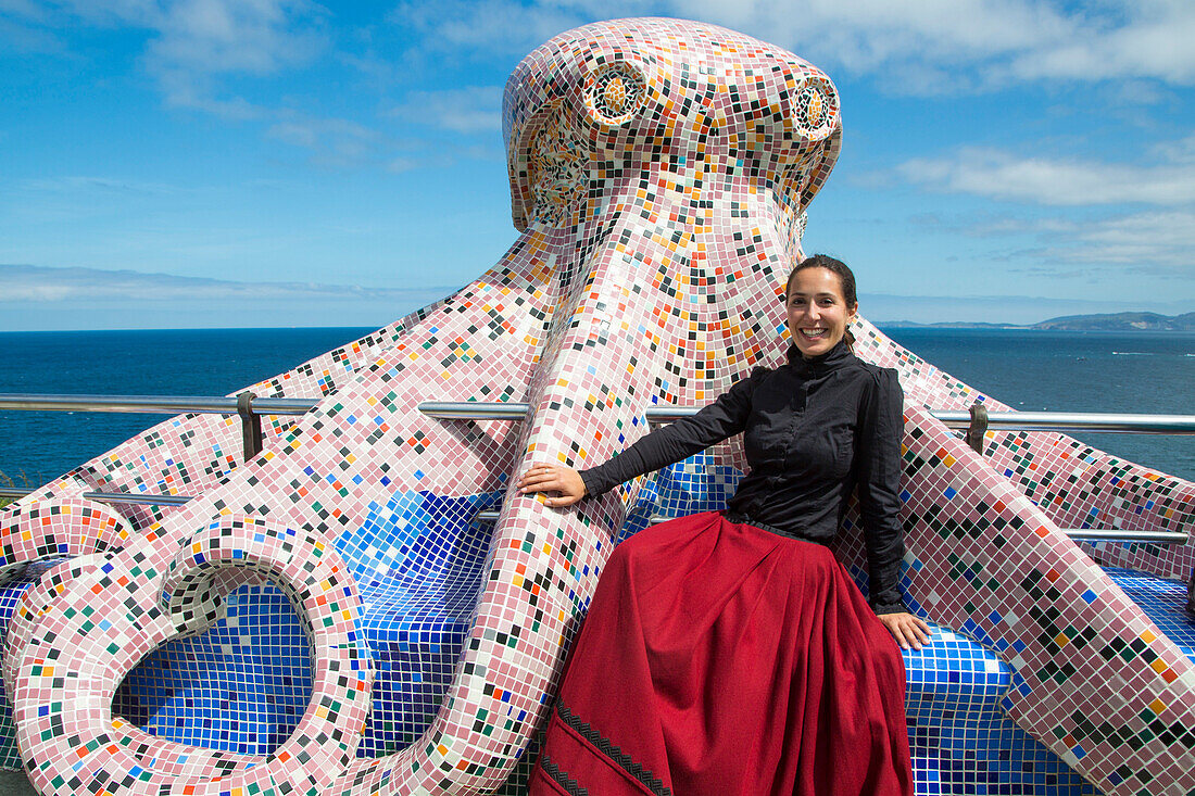 Frau in traditioneller Tracht sitzt auf Mosaikskulptur in Form von Oktopus, La Coruna, Galicien, Spanien, Europa