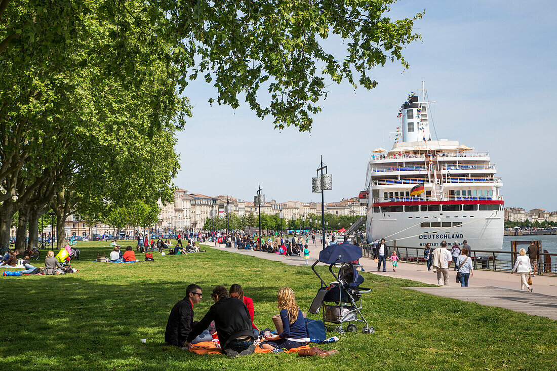 Menschen genießen einen sonnigen Sonntag im Park mit Kreuzfahrtschiff MS Deutschland (Reederei Peter Deilmann) am Ufer von Fluss Garonne, Bordeaux, Gironde, Aquitanien, Frankreich, Europa
