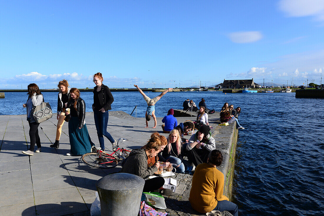 Young people sitting on the banks of the river Corrib, Galway, Ireland