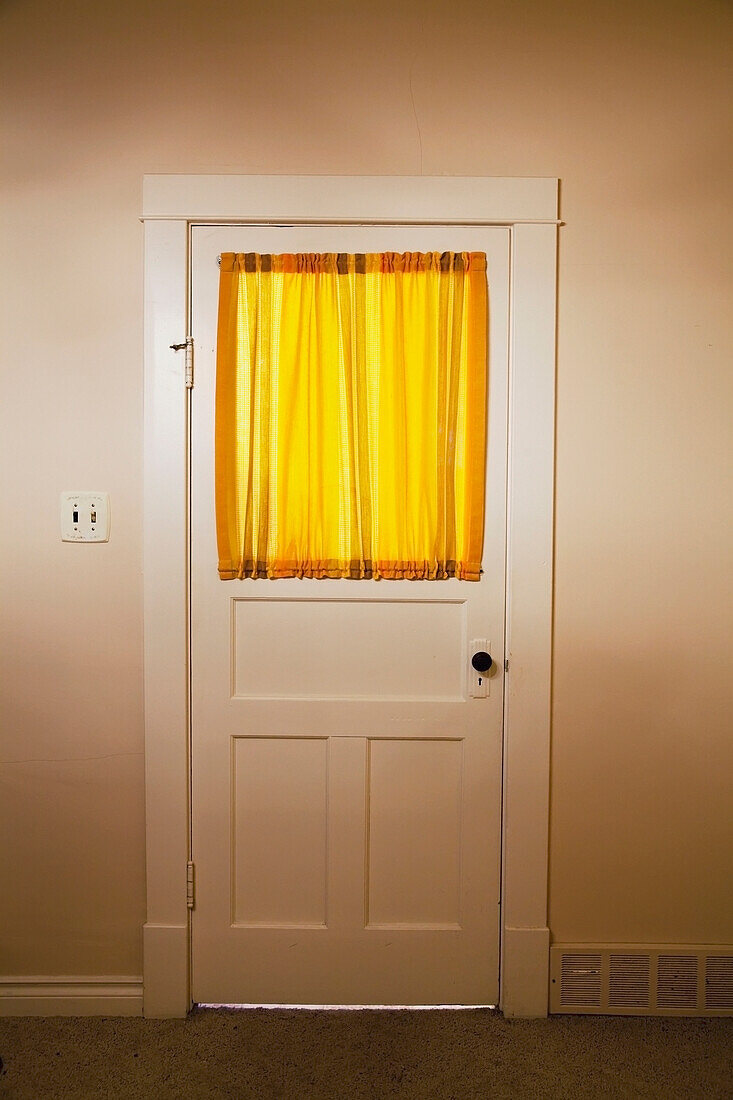 'Interior door of a 1920's farmhouse with yellow curtains on the window;Parkland county alberta canada'