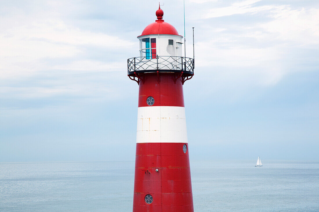 'Red and white lighthouse along the coast with a sailboat in the distance near westkapelle;Zealand, netherlands'