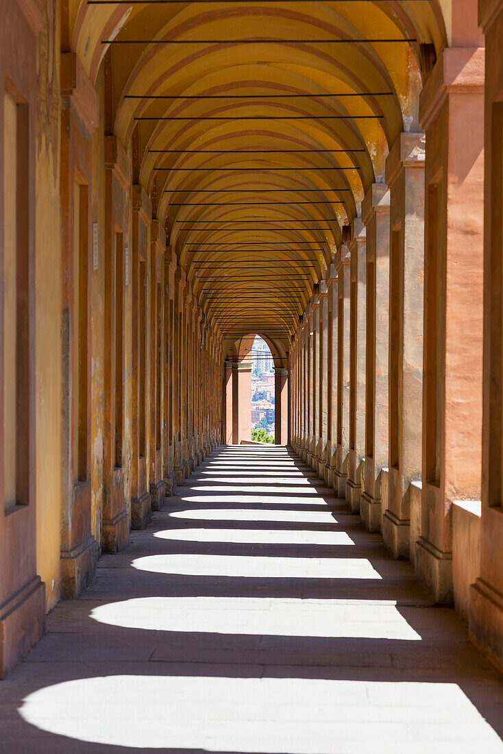 An outside corridor with arched roof and shadows of arches cast on the ground