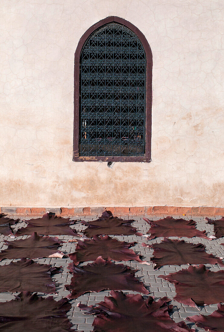 Animal skin mats in a row on the ground facing a wall with a screened window