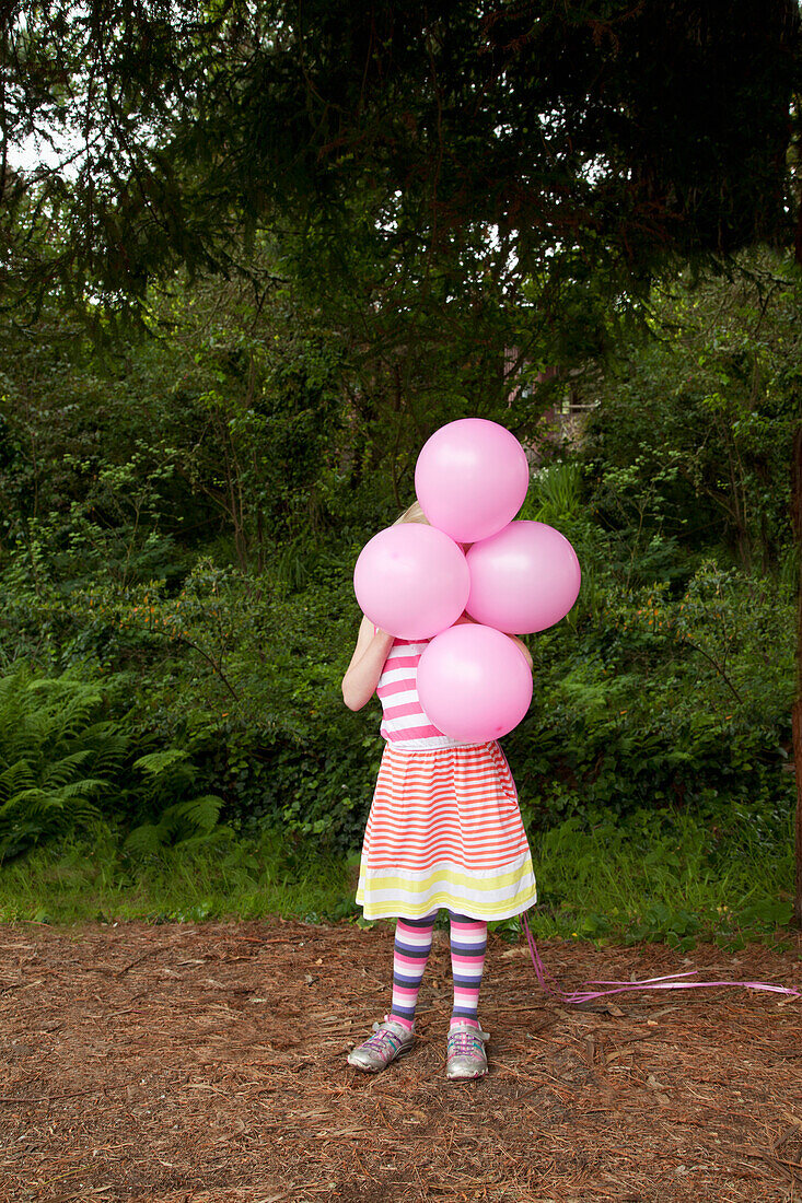 'A girl holding pink balloons in front of her face;Pacifica california united states of america'