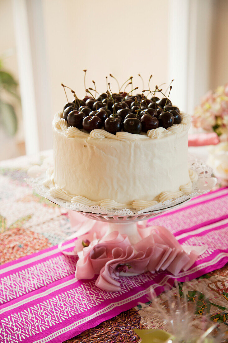'A white iced cake topped with fresh cherries on a pink table runner;California united states of america'