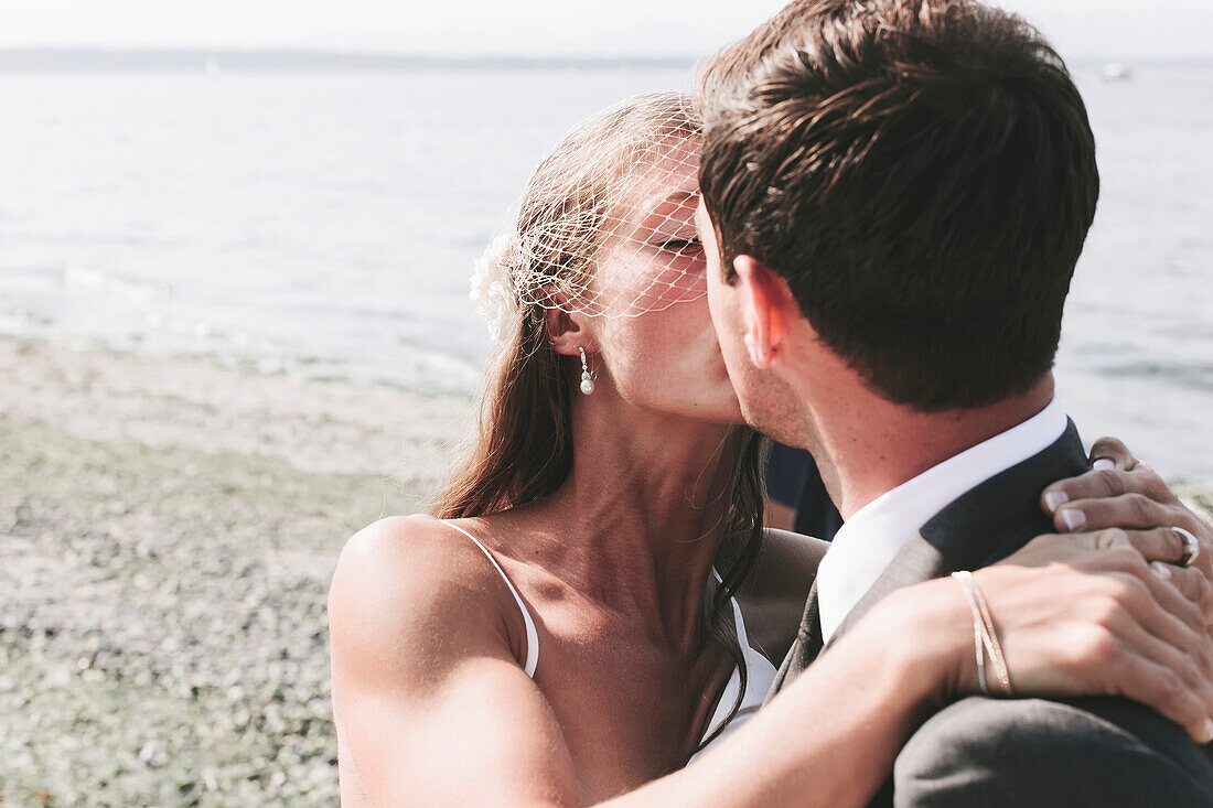 'A bride and groom kissing on a beach at the water's edge;Kirkland washington united states of america'