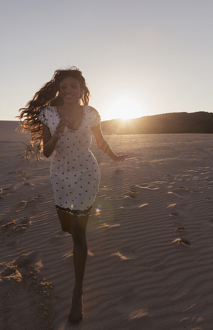 Eine junge Frau mit langen Haaren, die bei Sonnenuntergang am Strand läuft; Tarifa, Cadiz, Andalusien, Spanien