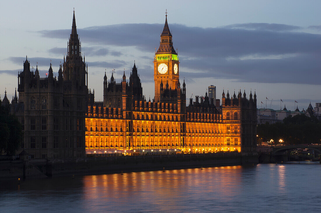 'A Building And Clock Tower Along The Water's Edge Illuminated At Dusk; London, England'