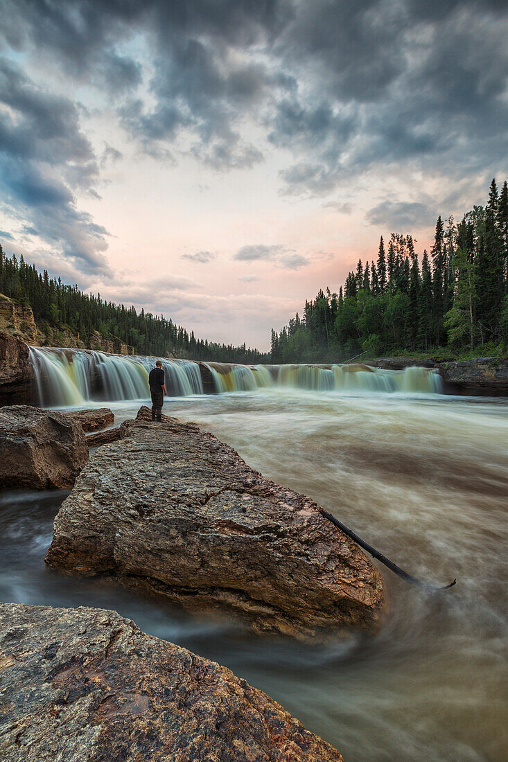 'A person watches as the Trout River flows over Sambaa Deh Falls in Sambaa Deh Territorial Park; Northwest Territories, Canada'