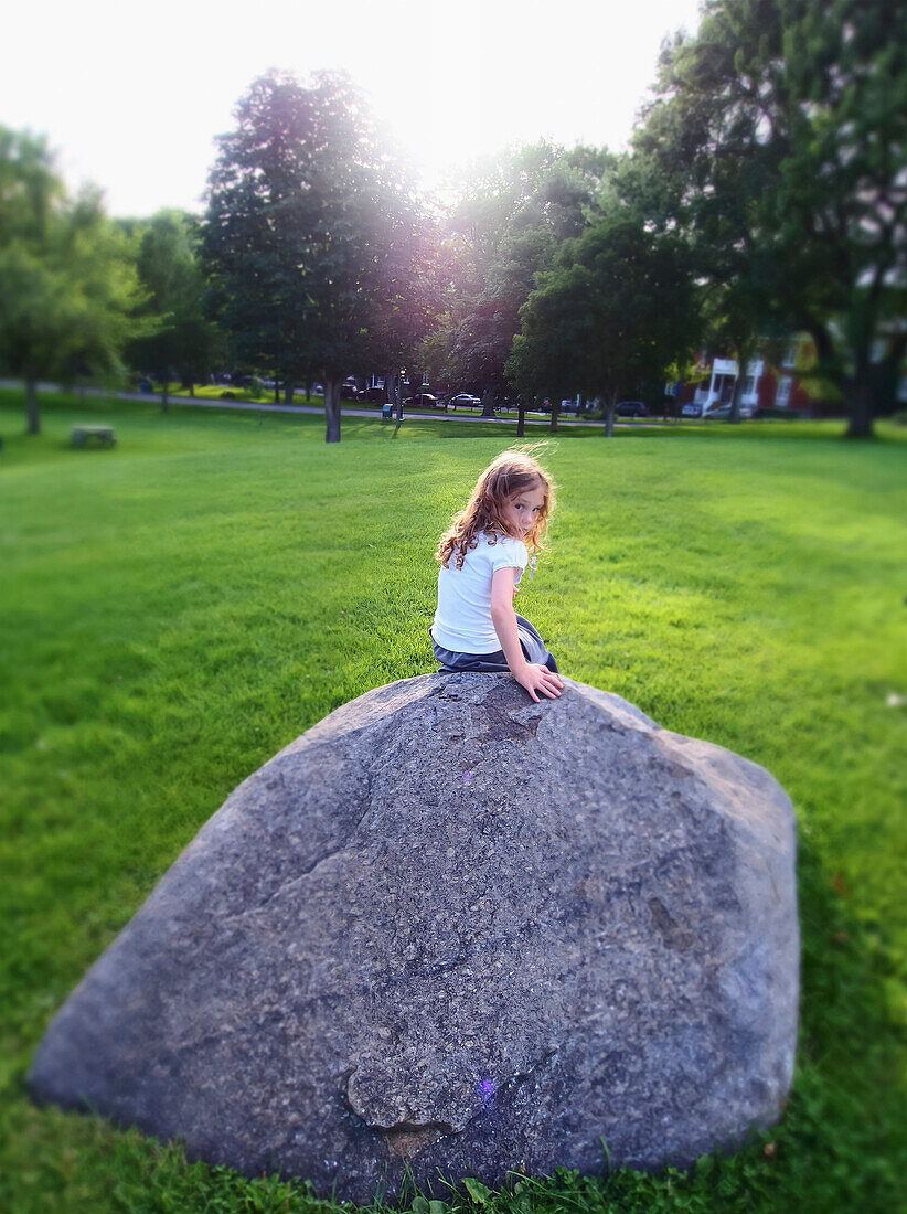 'A girl sitting on a rock in the Plains of Abraham city park on a summer day; Quebec City, Quebec, Canada'
