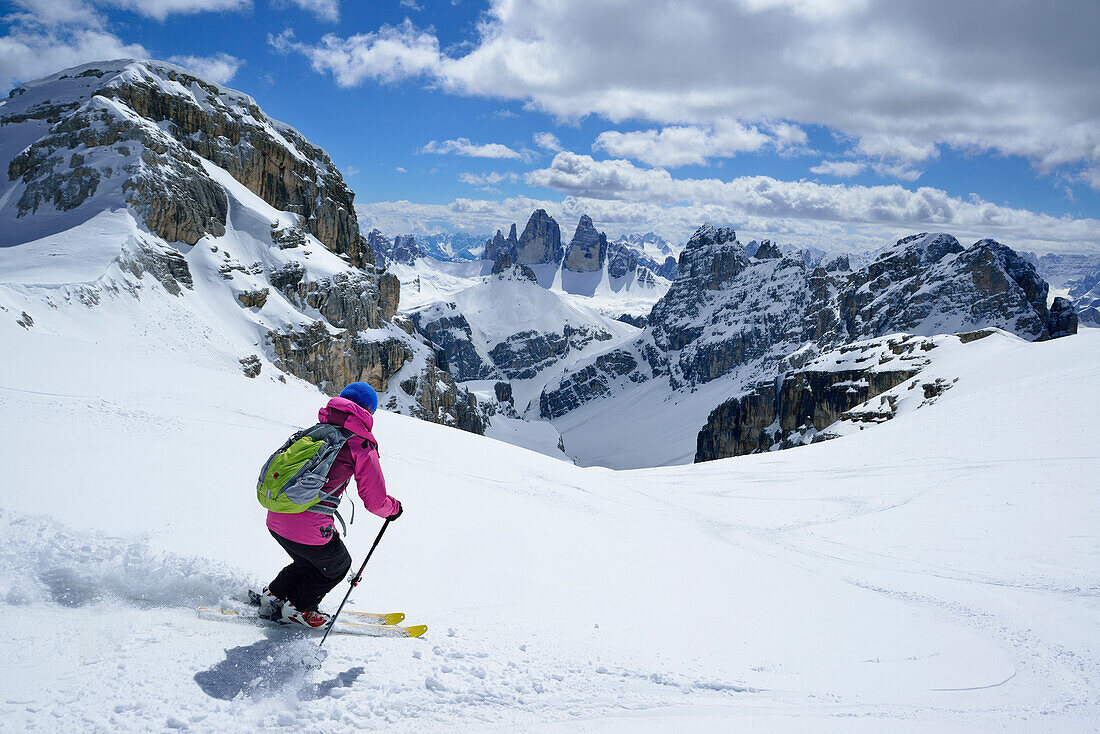 Frau auf Skitour fährt vom Hochebenkofel ab, Drei Zinnen im Hintergrund, Sextener Dolomiten, Südtirol, Italien
