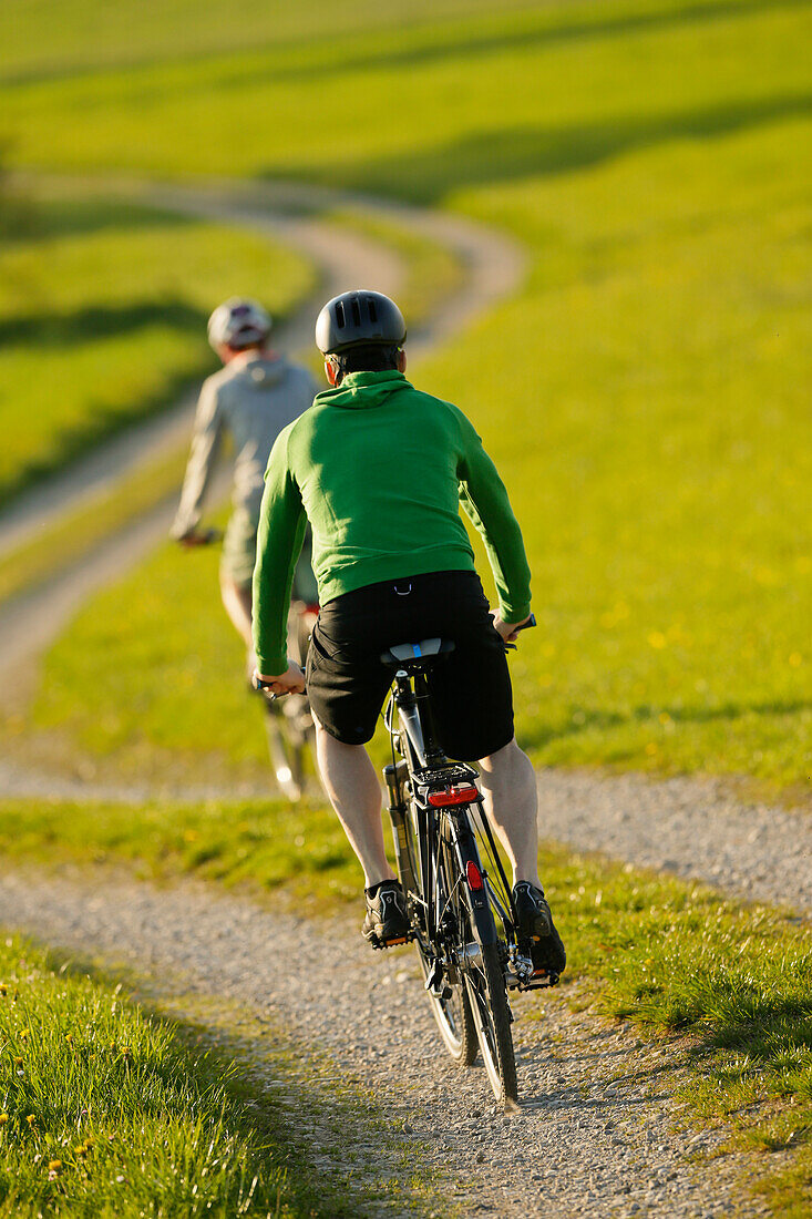 Two cyclists riding e-bikes, Munsing, Upper Bavaria, Germany