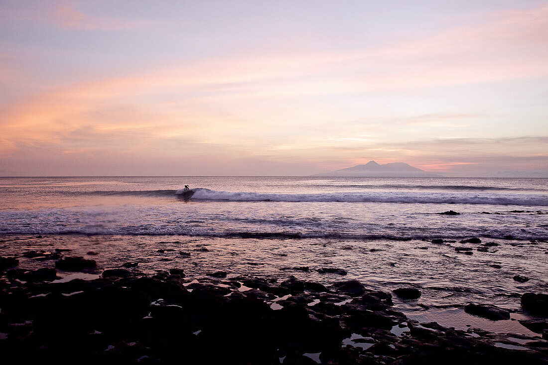 Surfer riding a wave in twilight, Praia, Santiago, Cape Verde