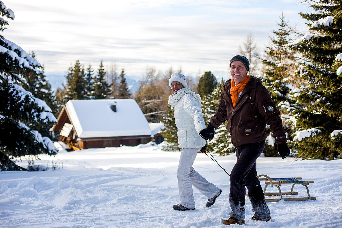 Paar mit einem Schlitten spaziert im Schnee, Mühlen, Steiermark, Österreich