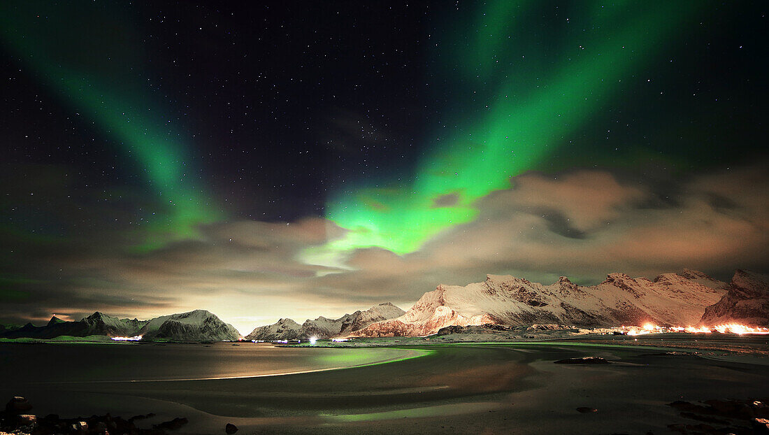 Spectacular Aurora Borealis in a Norwegian fjord. In the background the snow-covered mountains, in the foreground  the beach and the sea with the Aurora Borealis reflected. Lofoten Islands, Norway