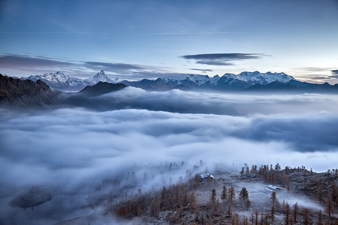 Fog covering Aosta valley at sunrise. Only the Matterhorn and the Monte Rosa emerge like islands from the sea of clouds, Mont Avic natural park, Aosta valley, Italy