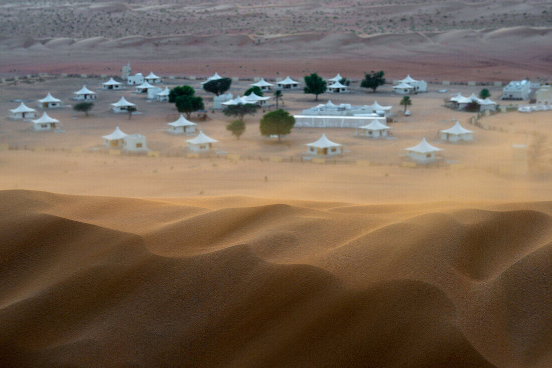 A photo of tented camp taken from the surrounding dunes with the wind lifts the sand of the desert Wahiba Sands in Oman.
