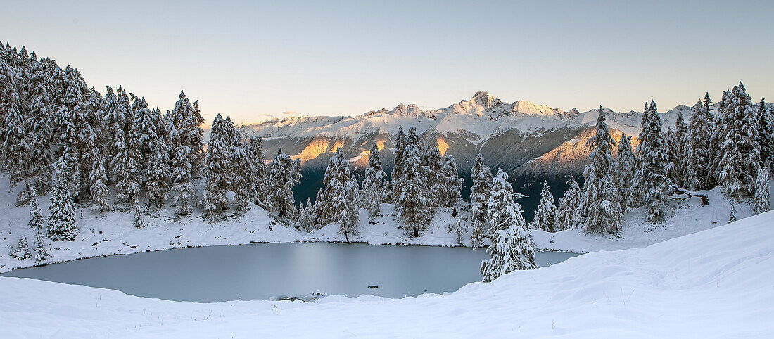 Panoramic view from an alpine lake, under the first autumnal snow, with mountains in the background, kissed by the first sunrise's lights, Orobie Alps, Valtellina, Lombardy