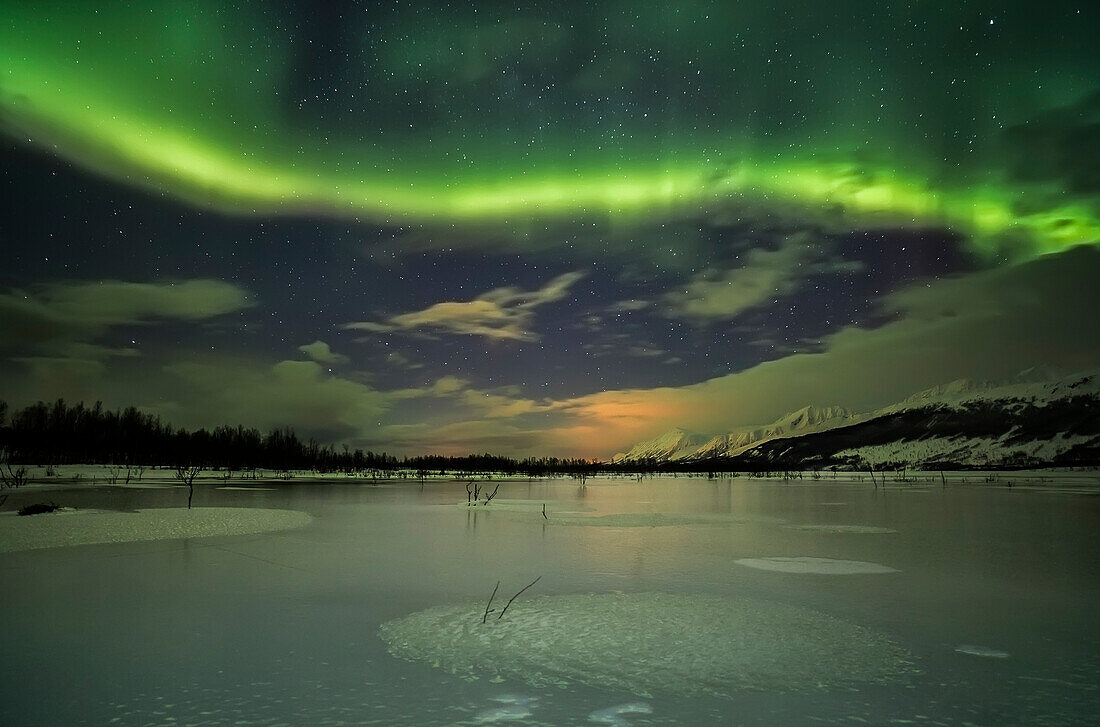 A frozen lake with norvegian alps in the background and, in the nocturnal sky, a beautiful aurora borealis, Norway